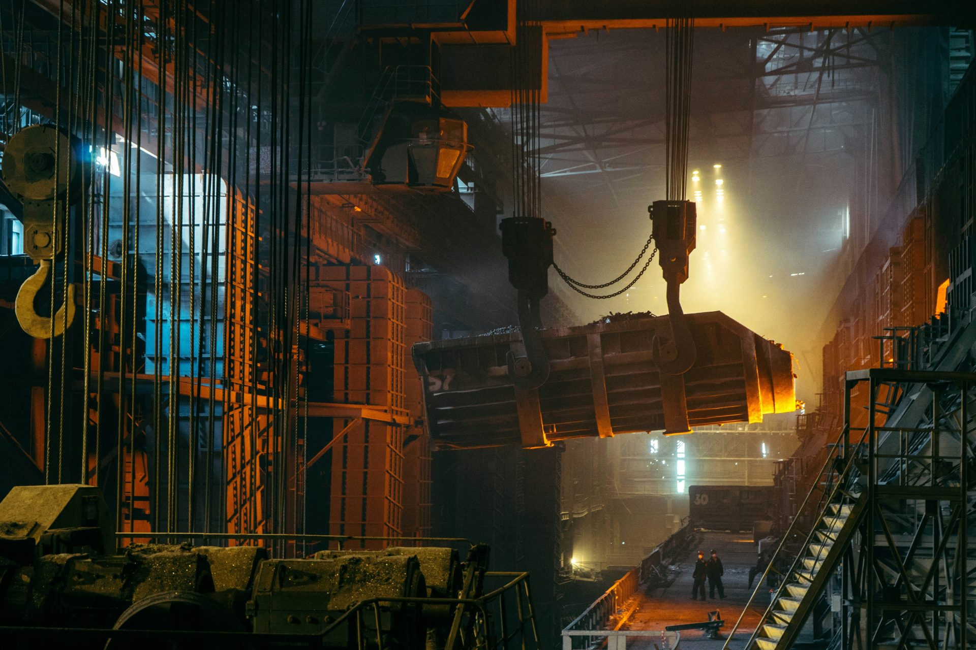 A heavy industrial crane lifting a glowing molten metal ladle in a steel mill